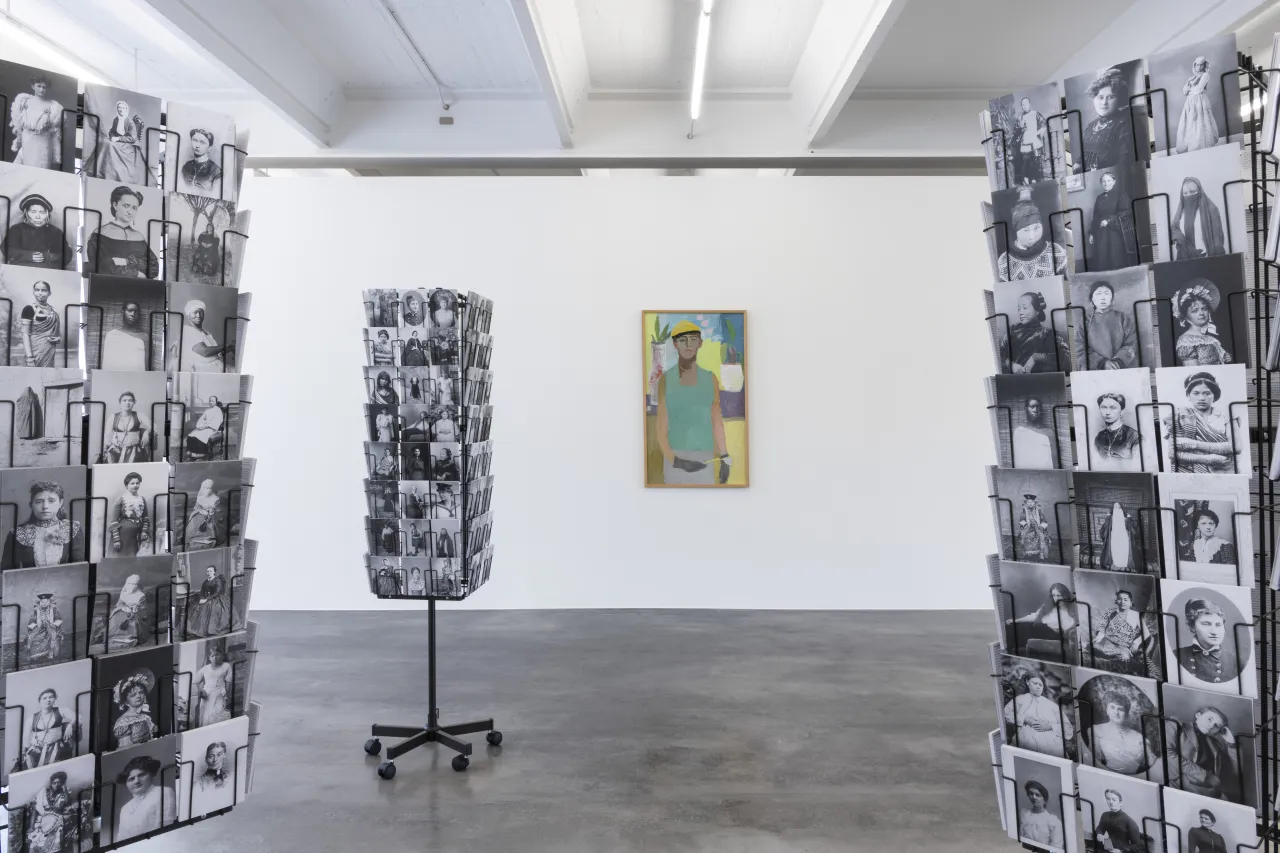 Installation view, foreground: Mathilde ter Heijne, "Woman* to Go", 2005 - ongoing, installation with free postcards, offset print, variable, background: Gudrun Irene Widmann, "Selbstbildnis", 1952, oil on hardboard, 120 x 70 cm, photo © Frank Kleinbach